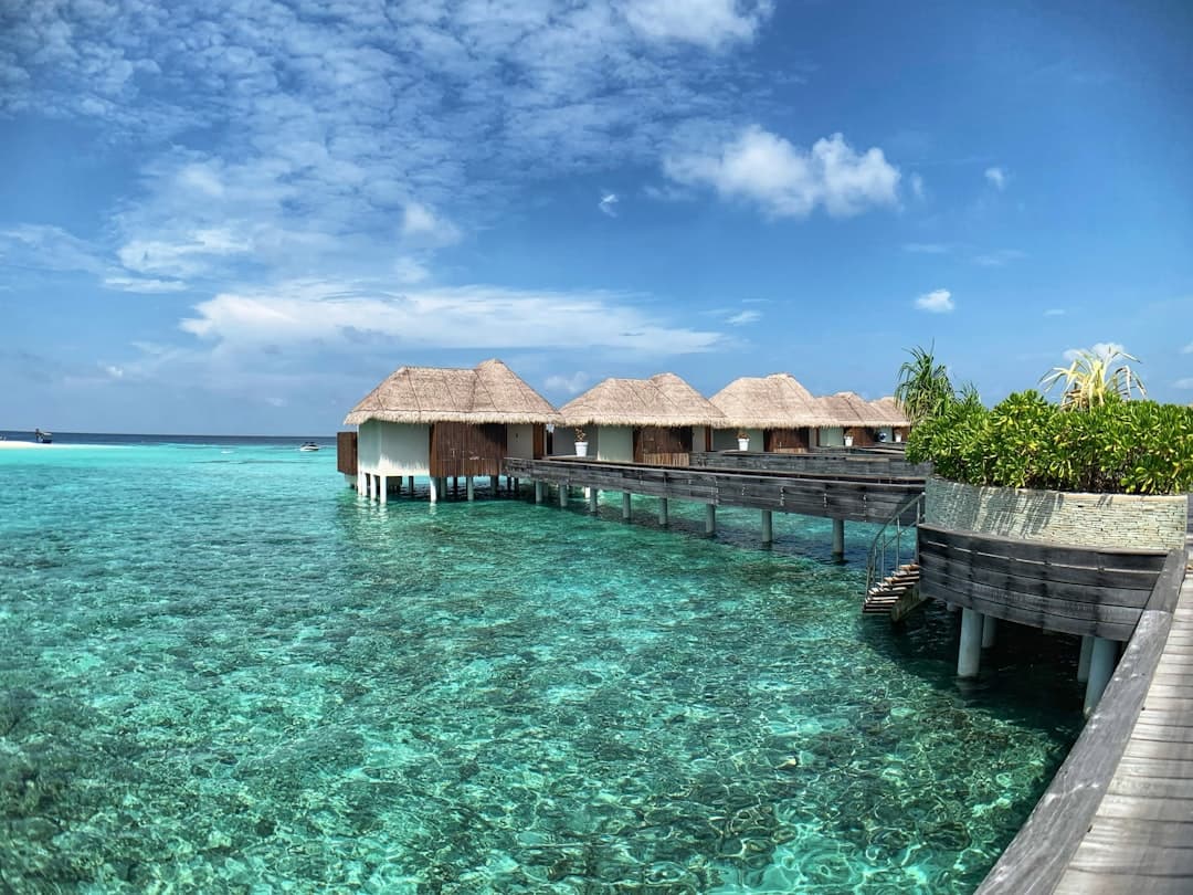 A luxury overwater resort with traditional thatched-roof bungalows connected by wooden walkways in crystal-clear turquoise lagoon waters, typical of Maldivian island resorts. - Photo by Upgraded Points on Unsplash