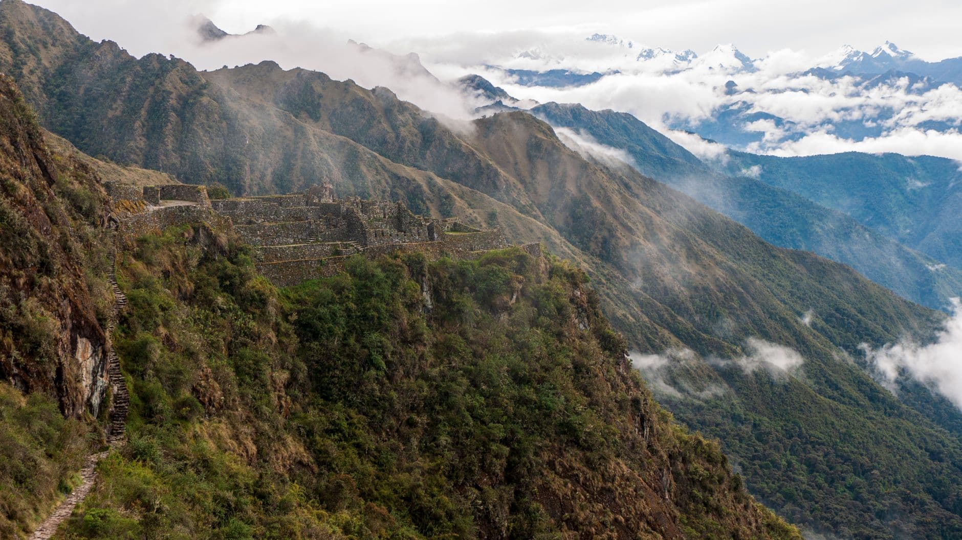 Inca stone ruins perched on a steep mountainside with terraced structures, flanked by dramatic Andean peaks shrouded in mist and cloud cover. - Photo by Wim Van den Brande on Pexels