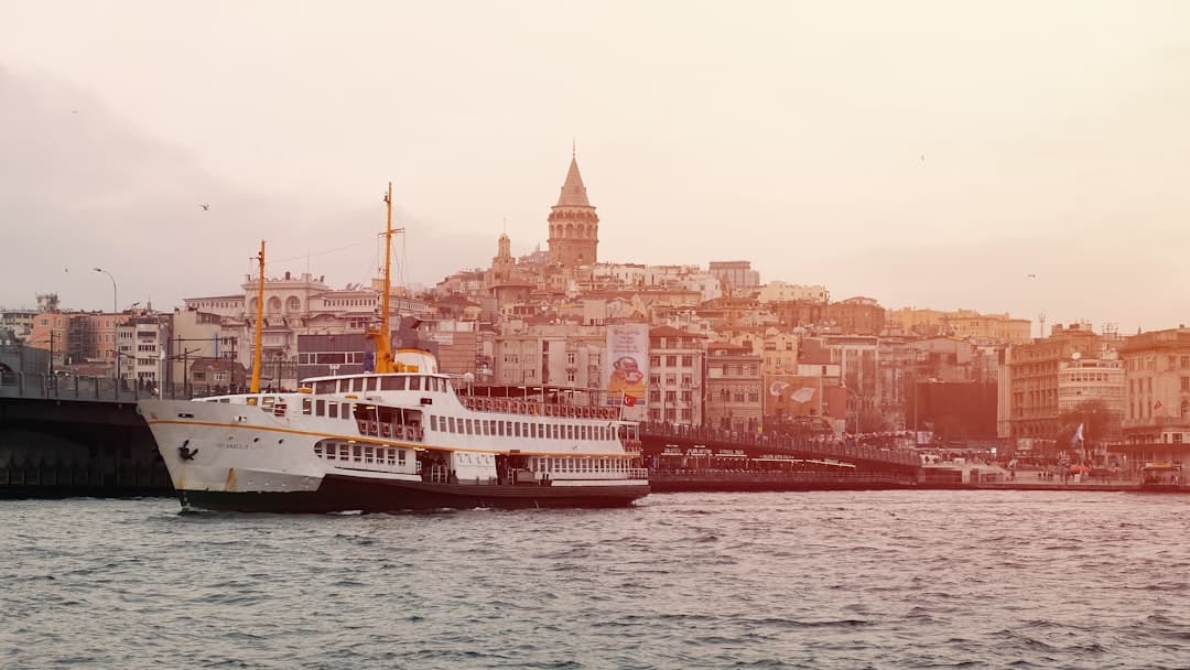 A white and red passenger ferry navigates the Golden Horn in Istanbul with the Galata Tower and historic Galata district visible on the hillside in the background. - Photo by Emre on Unsplash