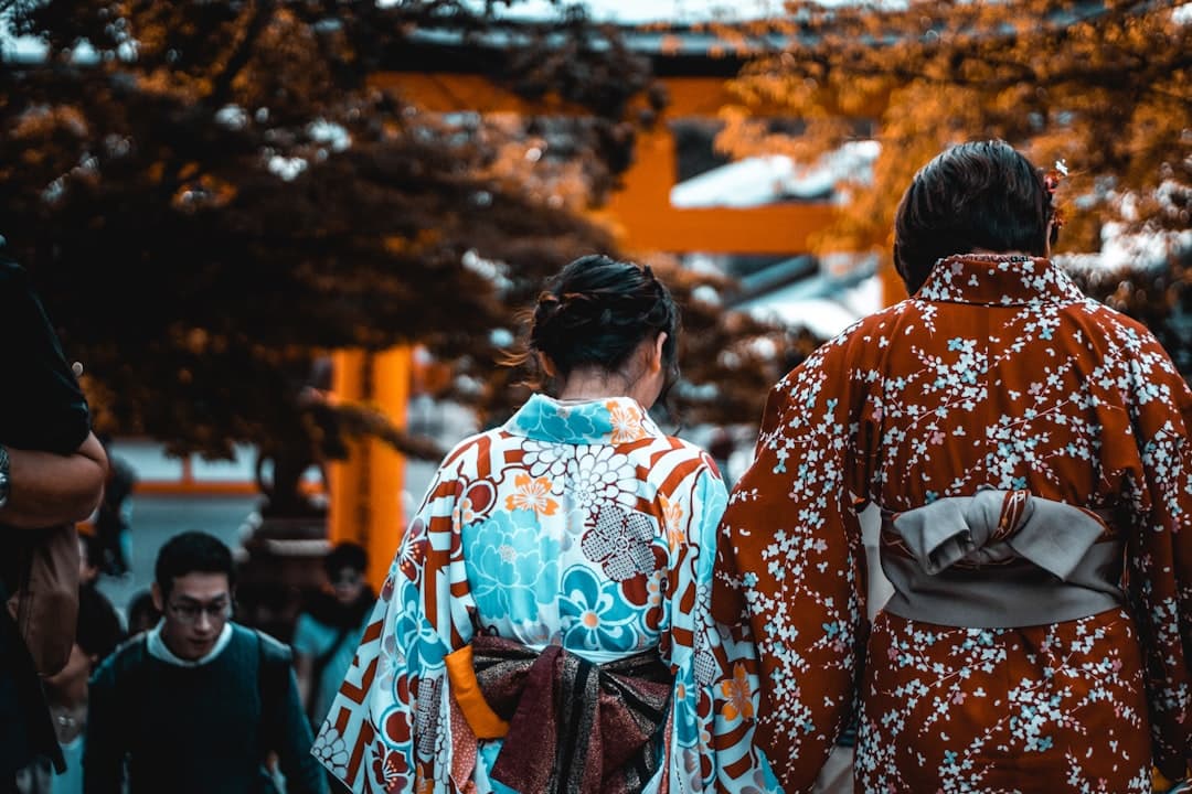 Two people wearing traditional Japanese kimono viewed from behind, standing in a snowy shrine setting with orange torii gates and snow-laden evergreen trees in the background. - Photo by Cosmin Georgian on Unsplash