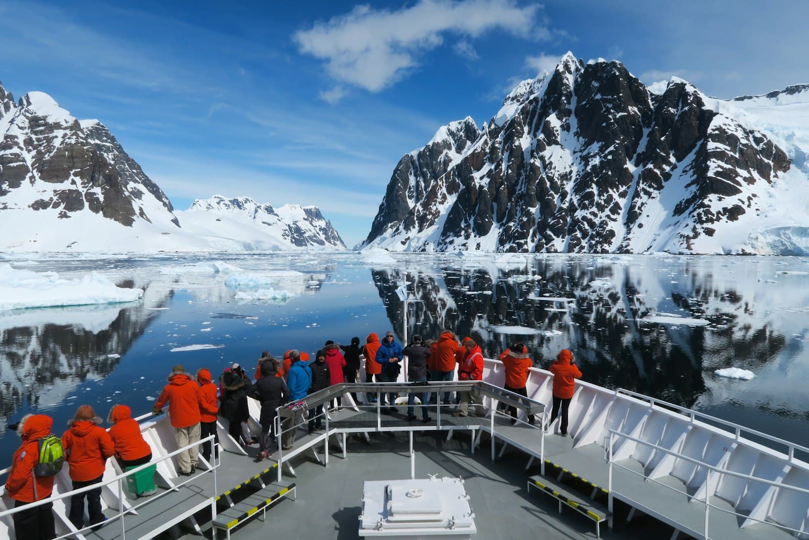 Passengers in bright expedition parkas observe snow-covered mountains and pack ice from the deck of a luxury expedition cruise ship navigating the Lemaire Channel in Antarctic Peninsula waters. - Photo by Freysteinn G. Jonsson on Unsplash