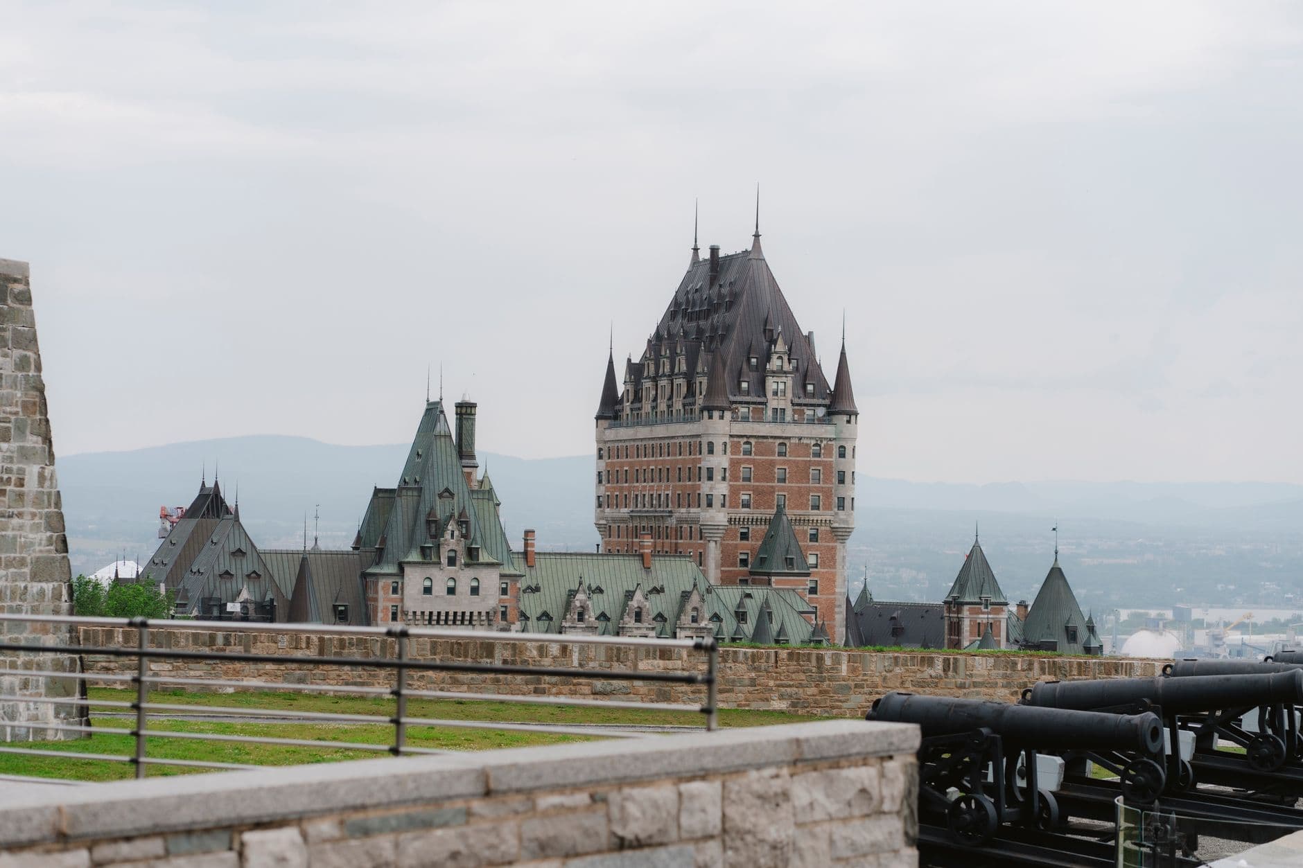 The Château Frontenac luxury hotel viewed from the Citadelle fortification, with period cannons and stone walls in the foreground overlooking the St. Lawrence River valley. - Photo by Valentina Rodriguez on Pexels
