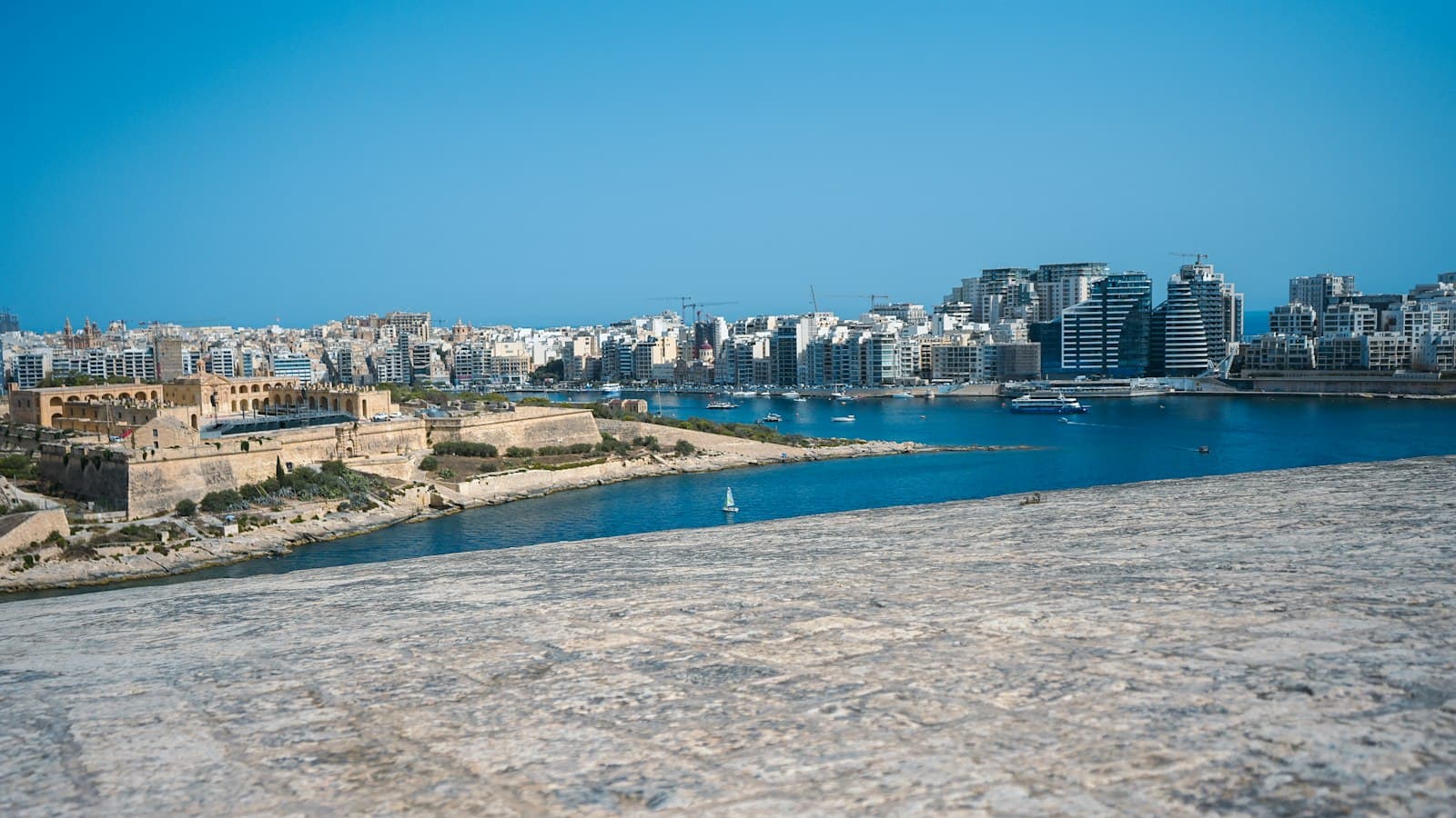 A view of Valletta's waterfront showing Fort St. Elmo in the foreground, the Grand Harbour with moored boats, and the city's skyline of historic and modern buildings rising steeply from the water's edge. - Photo by Damir Korotaj on Unsplash