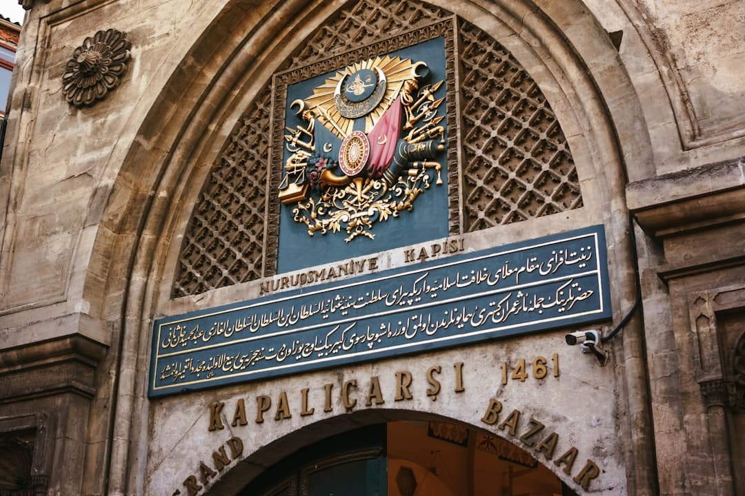 The Nuruosmaniye Gate entrance to Istanbul's Grand Bazaar (Kapalı Çarşı), featuring Ottoman imperial heraldry, ornate carved stonework, and bilingual Turkish/Arabic signage identifying this historic 18th-century gate. - Photo by Igor Sporynin on Unsplash