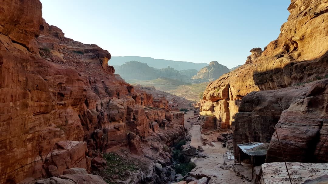 A canyon carved through red and golden sandstone with traditional Berber-style dwellings built into the rock faces, showing a winding path through a dramatic arid landscape with distant mountains. - Photo by Matt Jones on Unsplash