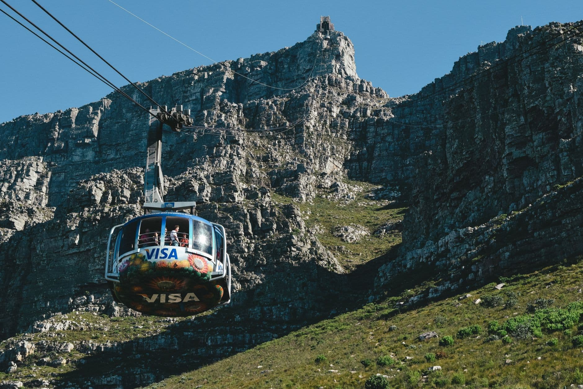 A rotating cable car ascending Table Mountain in Cape Town, with dramatic rocky cliffs and green vegetation visible in the background. - Photo by Tim Gouw on Pexels