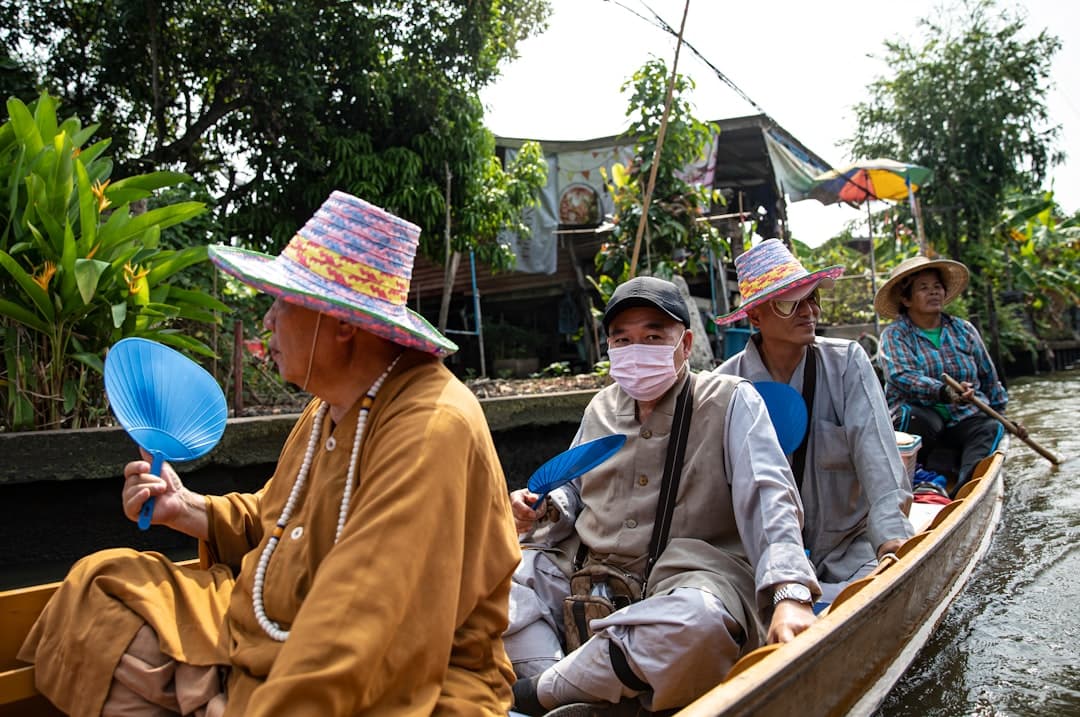 Tourists in a traditional wooden sampan boat with local Vietnamese boatmen wearing conical hats and traditional clothing, traveling through a narrow Mekong Delta waterway lined with tropical vegetation and stilt houses. - Photo by Leo_Visions on Unsplash