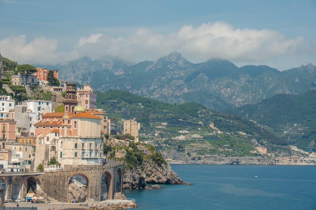 A picturesque coastal village built into a steep clifftop, featuring colorful Mediterranean architecture cascading down to turquoise waters, with dramatic limestone mountains rising behind, taken from sea level looking up at the settlement. - Photo by Line Kjær on Unsplash